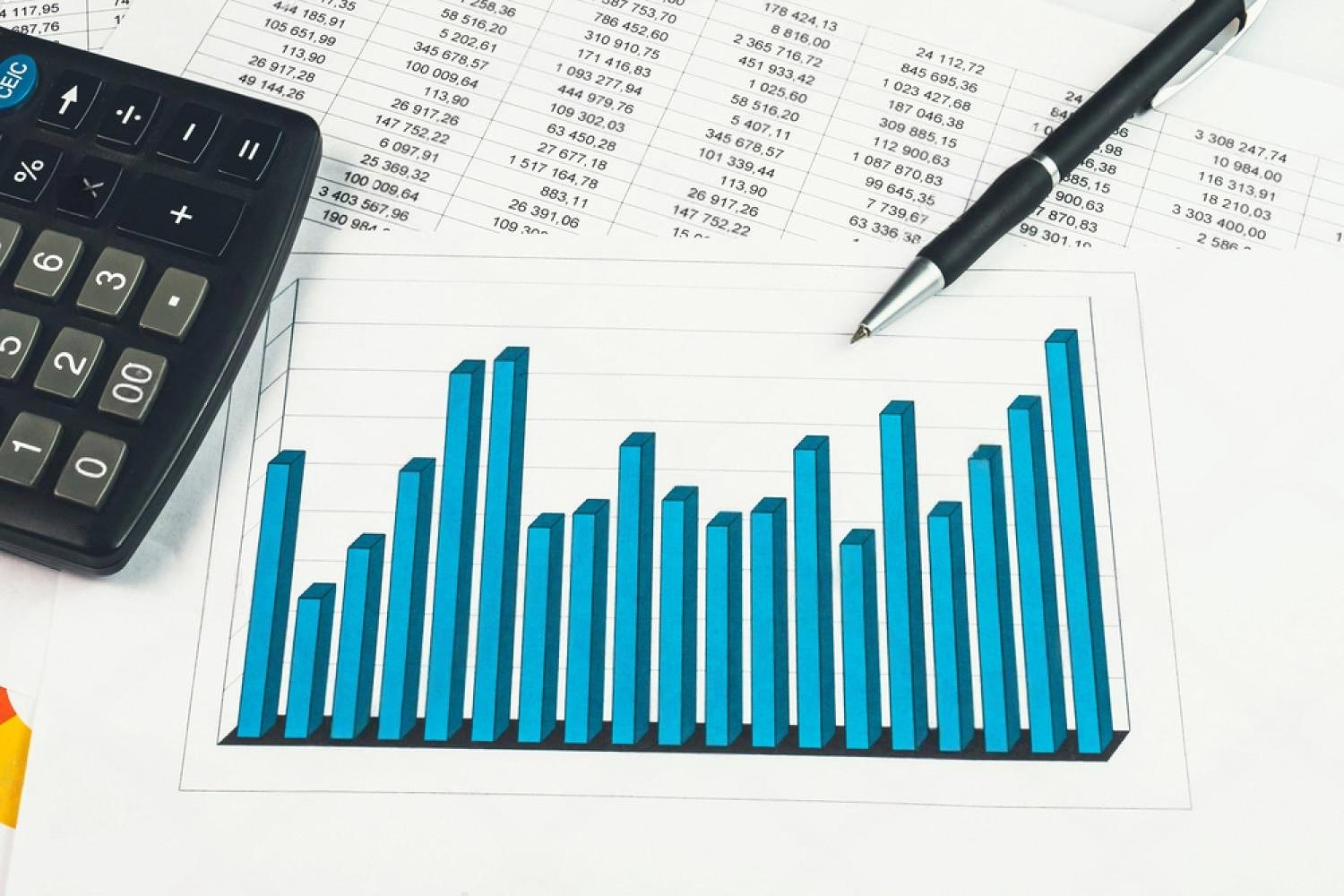Calculator and pen on a printed spreadsheet with a blue bar chart used in hidden asset analysis