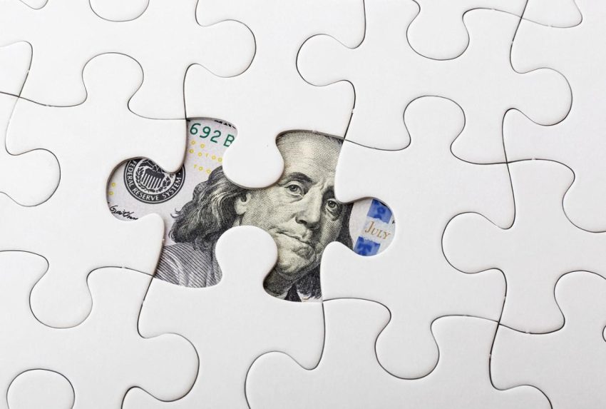 White puzzle with a missing piece revealing a US hundred dollar bill, symbolising hidden assets
